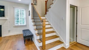 A staircase with wooden steps and a wooden handrail, leading to a landing with a black tufted bench. - Easy I-20 Access: Family Escape w/ Deck in Decatur (Decatur)