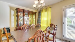A dining room with a large wooden table, six chairs, a chandelier, and a cabinet with glass doors.