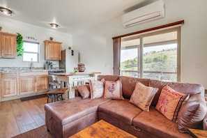 Una cocina moderna con armarios de madera, un comedor con sofá de cuero marrón y un ventanal con vistas a un paisaje montañoso.