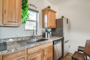Una cocina con armarios de madera, un refrigerador de acero inoxidable, un lavamanos y una ventana con una planta.