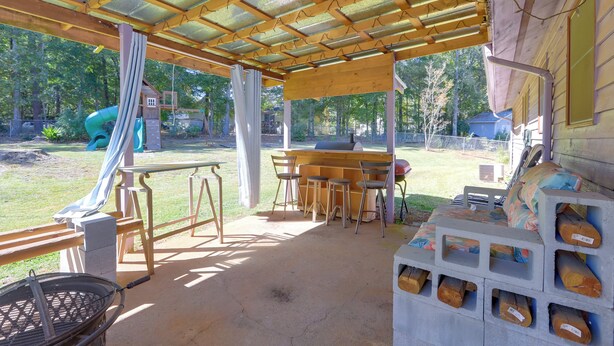 An outdoor patio with a wooden pergola, a barbecue area, and a play structure in the background. - Playground & Grill: Pet-friendly Griffin Getaway! (Griffin)