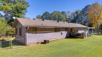 A single-story cabin with a covered porch, a fenced yard, and a clear sky.