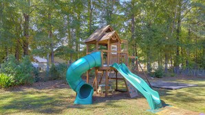 A wooden play structure with a slide and a small house-like building. - Playground & Grill: Pet-friendly Griffin Getaway! (Griffin)