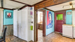 Une pièce avec un plafond en bois, une armoire blanche, un vase vert, une porte rouge et un réfrigérateur blanc.