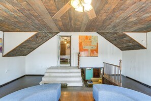 Une pièce avec un plafond en pente, un escalier menant à un niveau supérieur et une vue sur ce niveau supérieur à travers une porte ouverte.