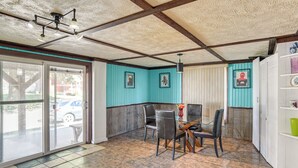 Un coin repas avec une table et des chaises en verre, un ventilateur de plafond et une vue sur l’extérieur grâce à une grande porte coulissante.
