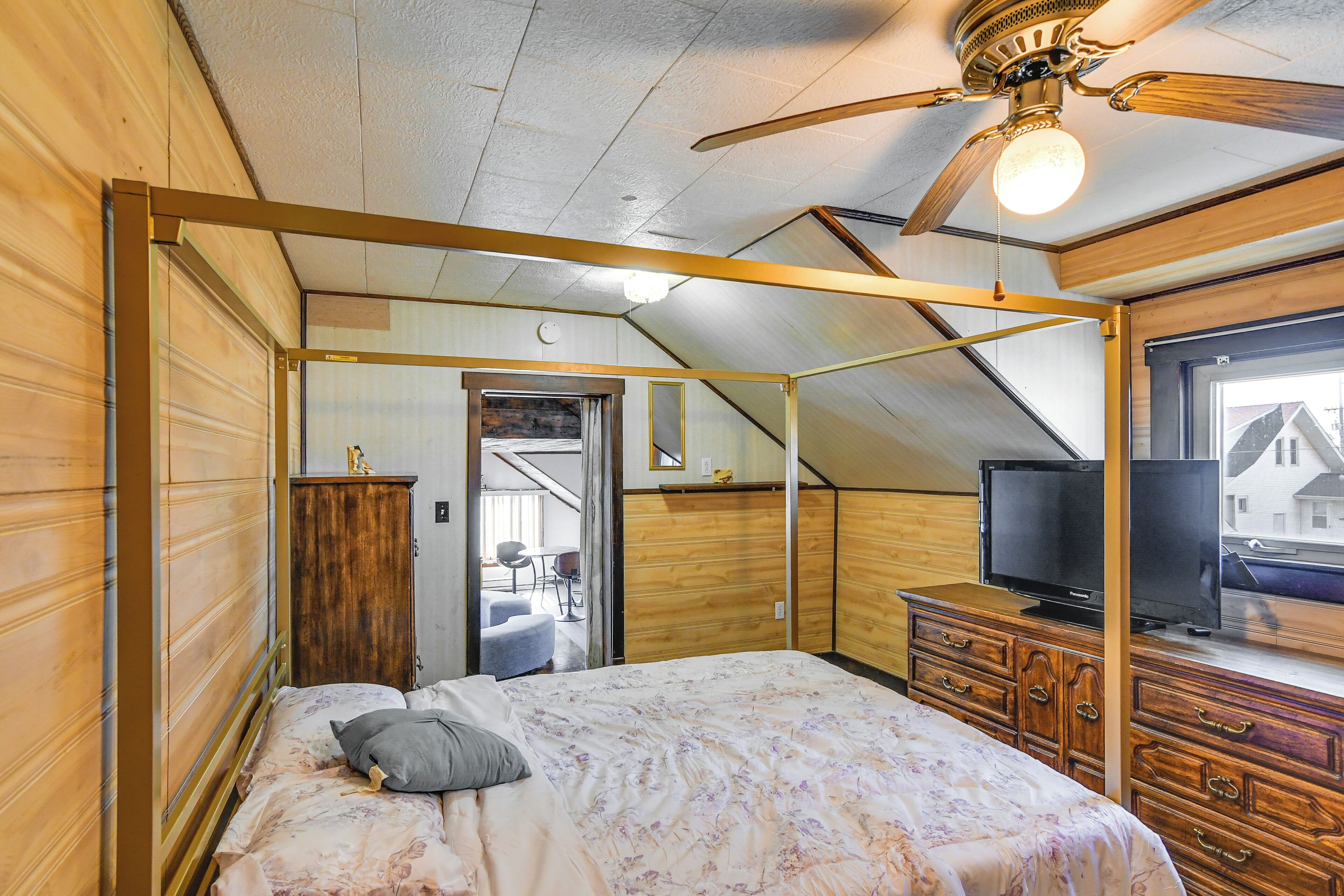 Een slaapkamer met een bed, een houten kledingkast, een televisie en een plafondventilator.