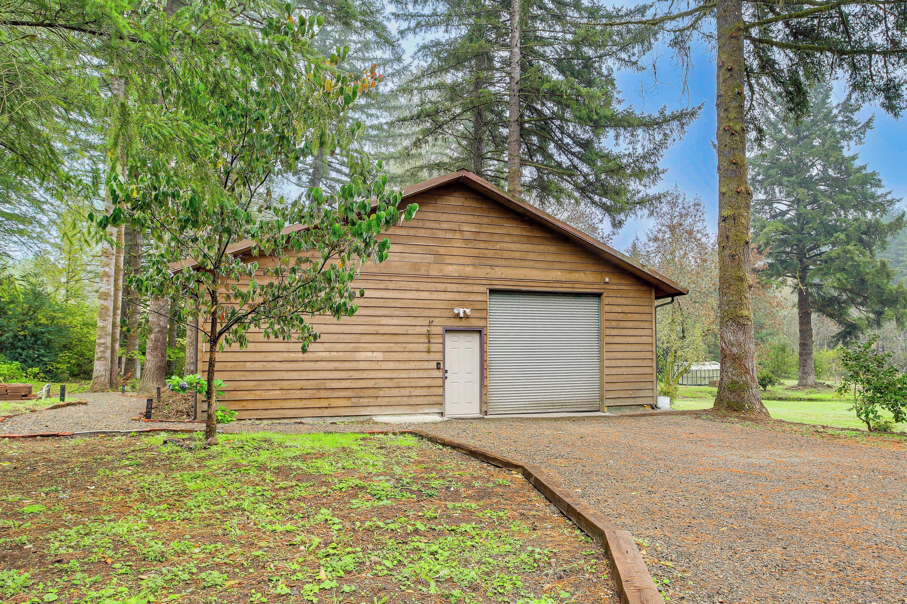 A wooden cabin with a garage, surrounded by trees and a gravel driveway.