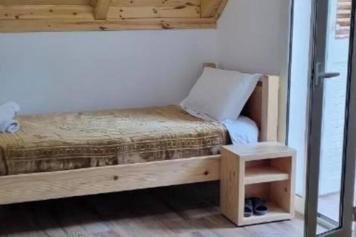 A bedroom with a sloped ceiling, wooden flooring, a bed with a patterned bedspread, a bedside table, and a small wooden nightstand.