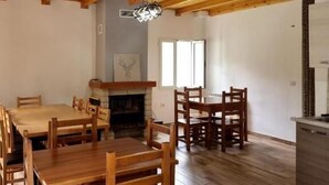 A spacious room with wooden flooring, a fireplace, and a dining area with wooden furniture. - Bujtina Tinari (Theth)