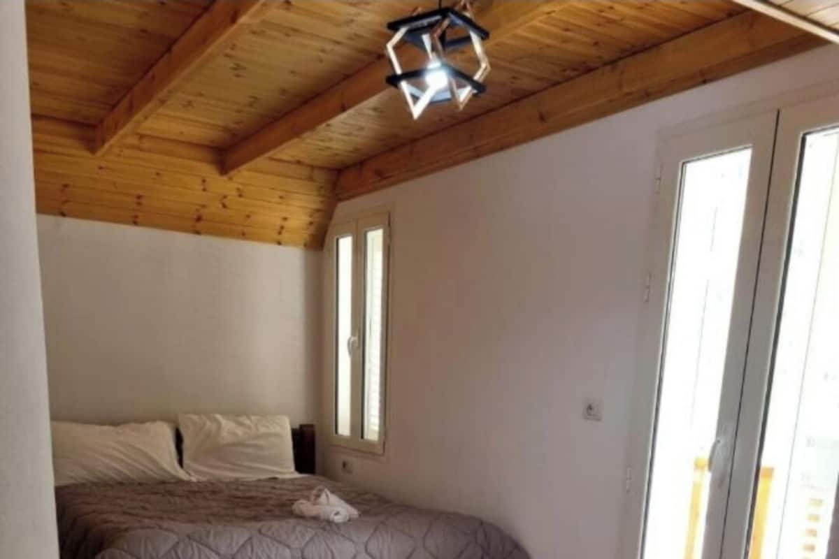 A bedroom with a wooden ceiling, two beds, and a large window.