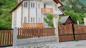 A two-story chalet with a stone facade, wooden balcony, and a view of a mountainous landscape. - Bujtina Tinari (Theth)