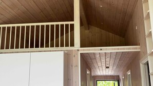 A wooden interior with a high ceiling, a white railing, and a view of greenery outside. - 5 Star Holiday Home in Vaeggerlose (Vaeggerlose)