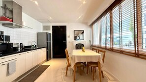 A compact kitchen with modern appliances, a dining area with a table and chairs, and a window with blinds. - B11 Sunset Plaza Partial Seaview 1 Bedroom 1 Bathroom With Large Jaguzzi (Karon)