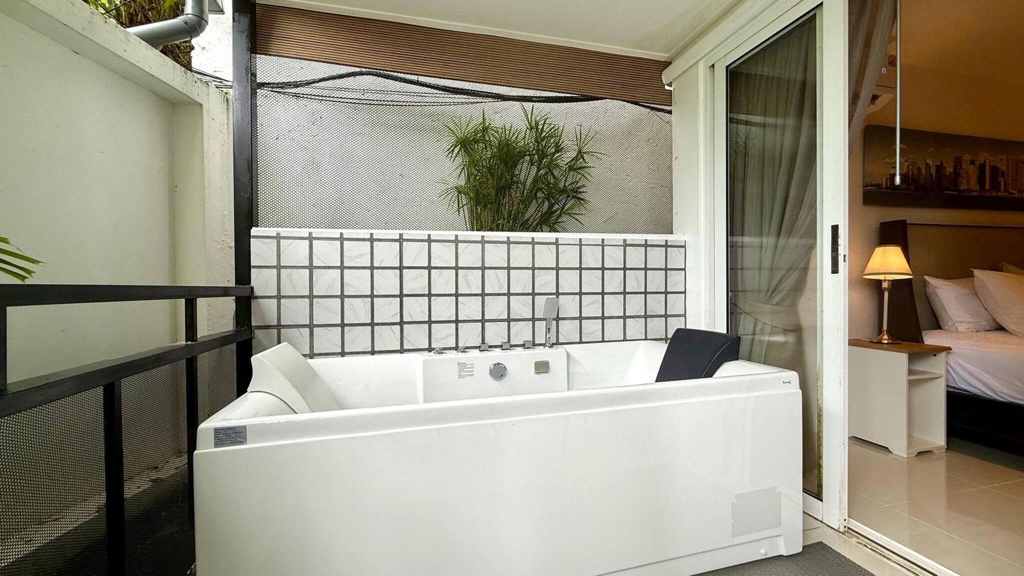 A modern bathroom with a white bathtub, a shower area, and a small bedside table with a lamp.