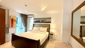 A hotel room with a bed, bedside lamps, a cityscape painting, an air conditioning unit, and a large mirror. - B11 Sunset Plaza Partial Seaview 1 Bedroom 1 Bathroom With Large Jaguzzi (Karon)