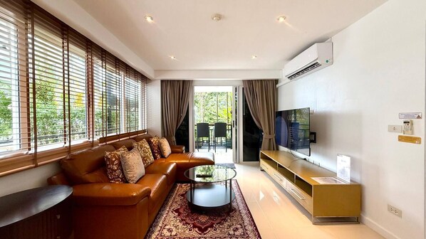 A modern living room with a leather sofa, a glass coffee table, and a flat-screen TV mounted on the wall. - B11 Sunset Plaza Partial Seaview 1 Bedroom 1 Bathroom With Large Jaguzzi (Karon)