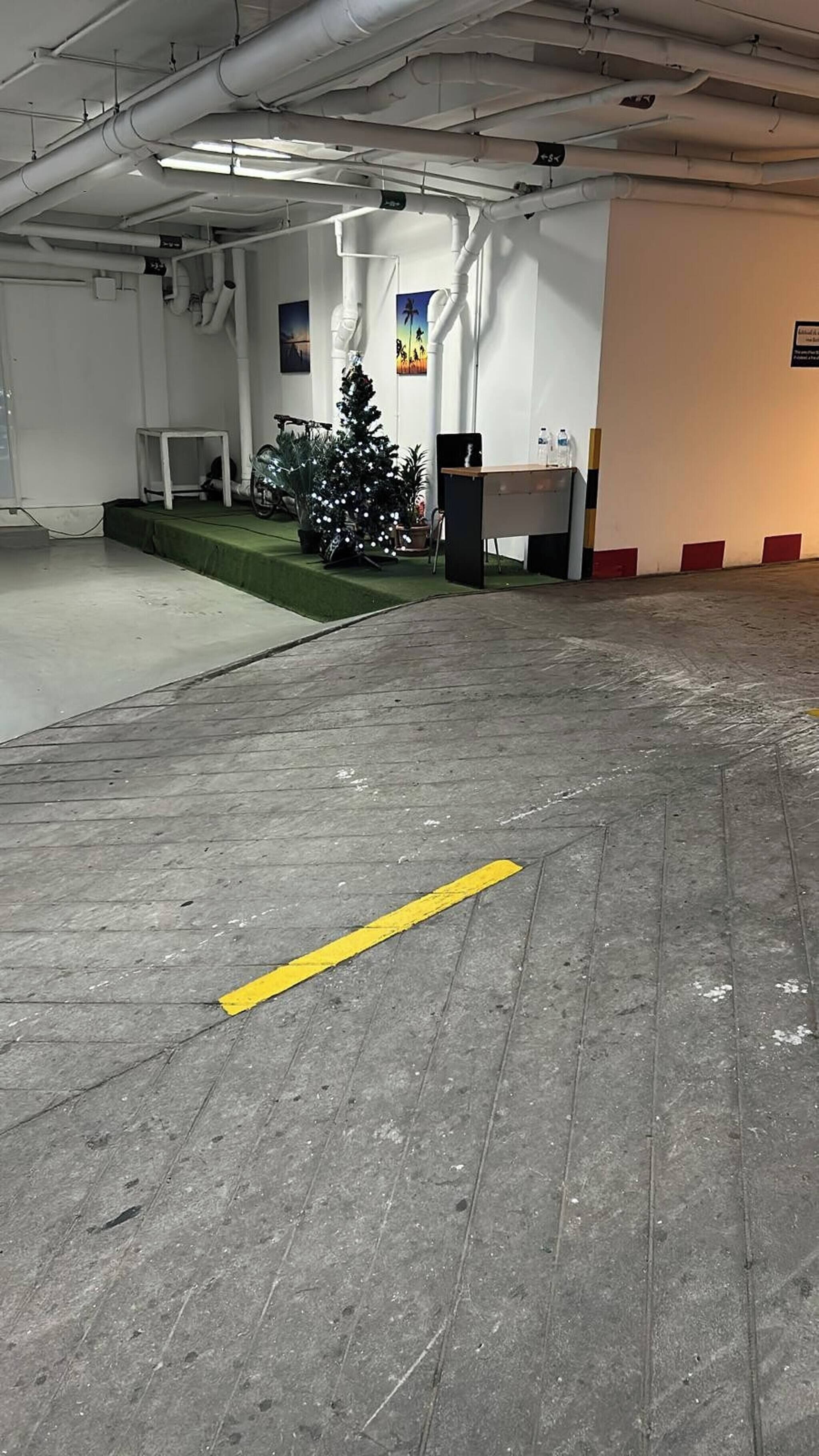 Un vaste espace de stationnement intérieur, délimité par une ligne jaune, où l’on trouve un sapin de Noël et une table avec des bouteilles.