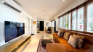 A modern living room with a flat-screen TV, a leather sofa, and a dining area with a table and chairs. - B11 Sunset Plaza Partial Seaview 1 Bedroom 1 Bathroom With Large Jaguzzi (Karon)