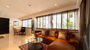 A modern living room with a leather sofa, a glass coffee table, and a dining area with a table and chairs. - B11 Sunset Plaza Partial Seaview 1 Bedroom 1 Bathroom With Large Jaguzzi (Karon)