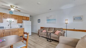 A compact living space with a kitchenette, a dining area, and a seating area with a sofa and armchairs. - Pelican Perch - Cozy Retreat, steps from the Ocean (Kure Beach)
