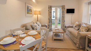 Un salon bien éclairé comprenant un coin repas, un ensemble de canapés, un téléviseur à écran plat et une vue sur l’extérieur, accessible par une porte vitrée.