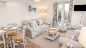Un salon moderne avec un canapé, une table à manger et des chaises. Un téléviseur est fixé au mur et il y a une fenêtre avec des rideaux.