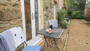 Un bâtiment en pierre doté d’un patio comprenant une table et des chaises, une bouteille de vin et un saladier de fraises.