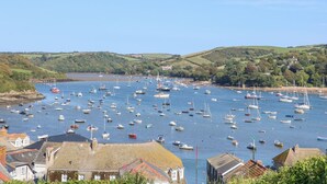 Une ville côtière où de nombreux bateaux sont amarrés dans un port, entourée de collines verdoyantes et de bâtiments à l’architecture traditionnelle.