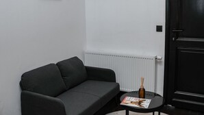 Ein dunkelgraues Sofa vor einer weißen Wand, ein kleiner runder Tisch mit einer Zeitschrift und eine schwarze Tür.