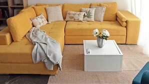 A living room with a yellow sofa, a white coffee table, and a bookshelf. - Near to Victoria. Cozy 2 bedroms penthouse with Citadel view. (Ta' Sannat)