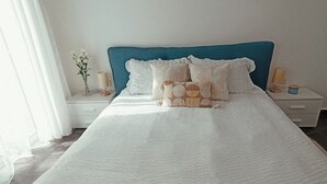 A neatly made bed with a blue headboard, white bedding, and decorative pillows. There are bedside tables with lamps and a vase of flowers. - Near to Victoria. Cozy 2 bedroms penthouse with Citadel view. (Ta' Sannat)