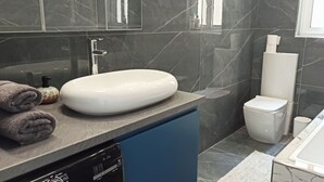 A modern bathroom with a white oval sink, a toilet, and a bathtub. - Near to Victoria. Cozy 2 bedroms penthouse with Citadel view. (Ta' Sannat)