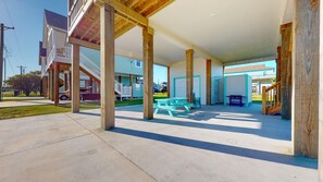 A covered outdoor area with picnic tables and a barbecue grill, wooden pillars, and a view of residential buildings.