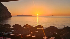 A sunset view from a beachside hotel with thatched umbrellas and lounge chairs. - Classic Quadruple Room 1 with Balcony and Air Conditioning (Perissa)