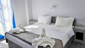 A bedroom with a bed, two bedside tables, a wall-mounted light, and a window with curtains. - Classic Quadruple Room 1 with Balcony and Air Conditioning (Perissa)