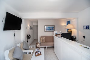 A compact living space with a flat-screen TV, a sofa, a small table, a lamp, and a framed picture on the wall.