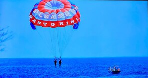 Un parachute ascensionnel sur lequel on peut lire les mots « Pleasure Santorini », deux personnes debout en dessous, et un bateau sur lâeau.