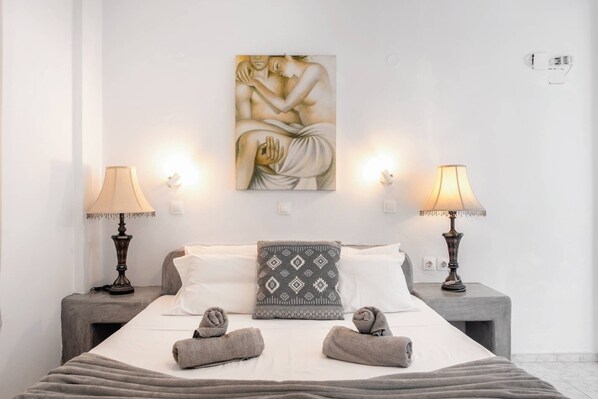 A neatly made bed with two pillows, two bedside lamps, and a wall-mounted painting.