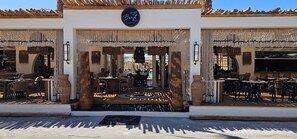 Un restaurante con terraza, un letrero sobre la entrada y un toldo decorativo.