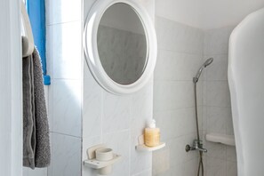 Ein Badezimmer mit rundem Spiegel, Dusche, Handtuchhalter und Seifenspender.