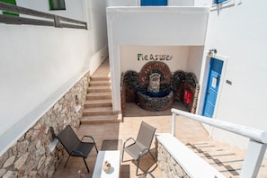 A narrow outdoor corridor with stone walls, a stone bench, a table with a vase, and a blue door. - Double Room with View 9 – Sea View, Balcony, and Air Conditioning (Perissa)