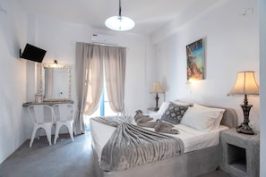 A bedroom with a bed, bedside lamps, a TV, a desk with chairs, and a window with curtains.