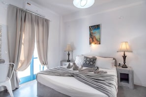A bedroom with a bed, two bedside lamps, a painting, and a window with curtains.