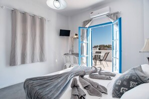 A hotel room with a bed, a TV, a desk, and a view of the outdoors. - Double Room with View 10 – Sea View, Balcony & Air Conditioning (Perissa)
