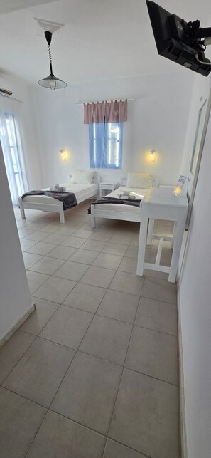 Een kamer met twee bedden, een bureau, een plafondventilator en een raam met gordijnen.