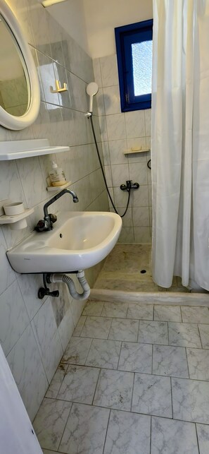 A bathroom with a sink, mirror, shower, and tiled floor.