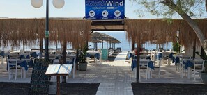 Un restaurante frente a la playa con terraza, un cartel de South Wind y vistas al mar.