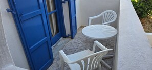 Ein kleiner Sitzbereich im Freien mit Tisch und zwei Stühlen, einer blauen Tür und einer weißen Wand.