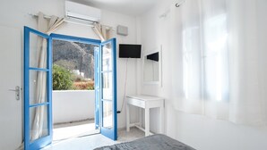 A bedroom with a bed, a desk, a chair, a TV, and an open door leading to a balcony. - Economy Quadruple Room 1 with Balcony and Air Conditioning (Perissa)